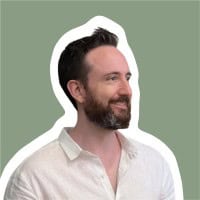 A bearded man with short dark hair smiles while looking to the right. He is wearing a white shirt and is outlined in white against a muted green background.