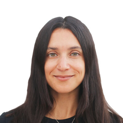 A person with long, dark hair smiles softly against a plain white background. They are wearing a black top and a silver necklace.