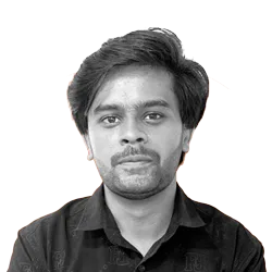 A young man with medium-length dark hair and facial hair, wearing a dark collared shirt, looks directly at the camera with a neutral expression. The background is removed.